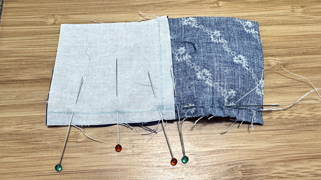 Two squares stitched together, pinned to another two. A threaded needle started going through the blue square.