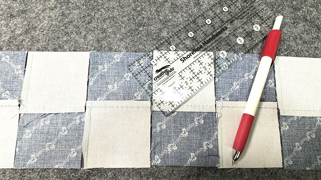 Several 2-patch side by site. A quilting ruler and a fabric pencil on top. All the stitch lines have been marked.
