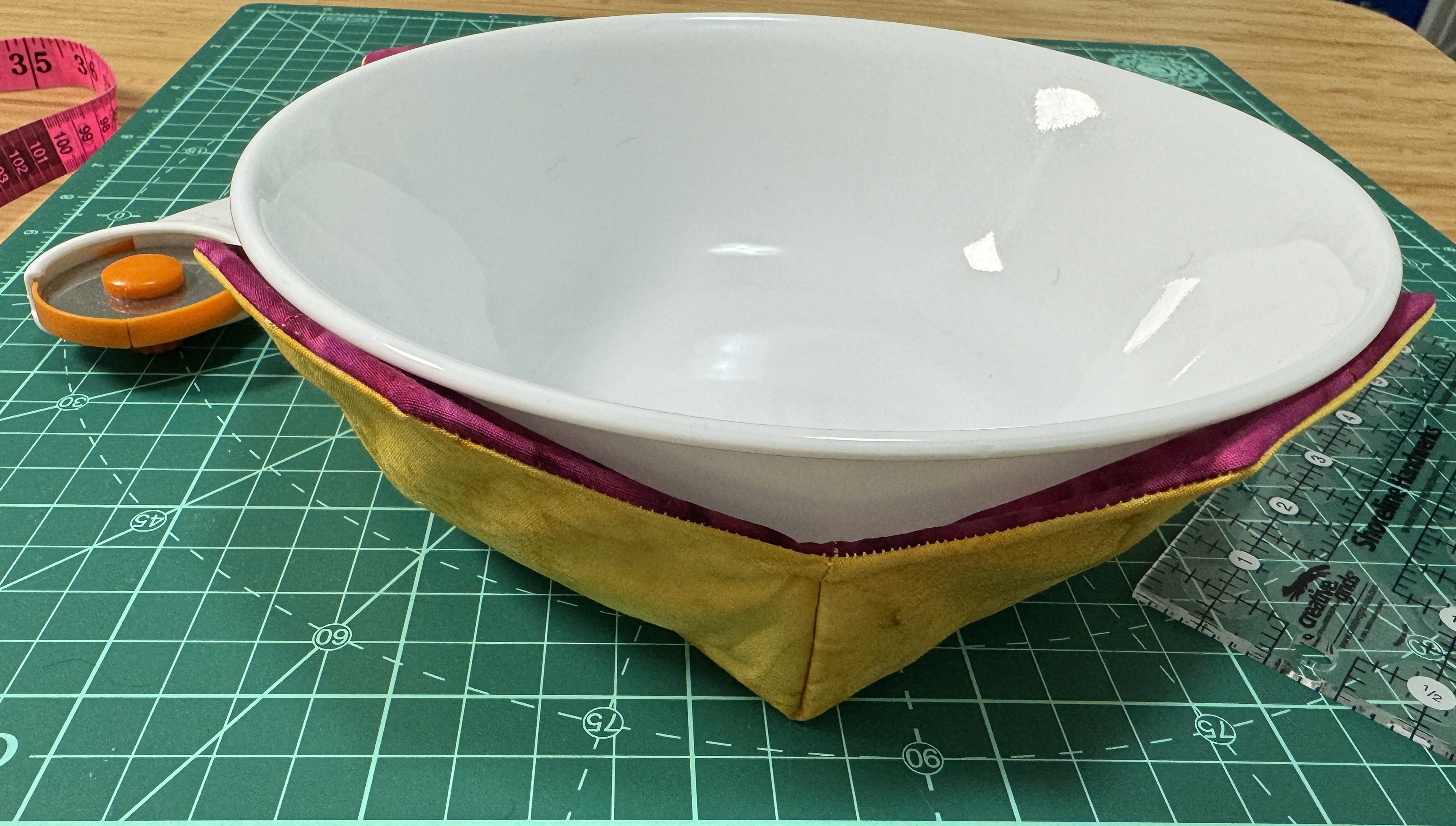 A large white bowl in a yellow and purple bowl cozy.