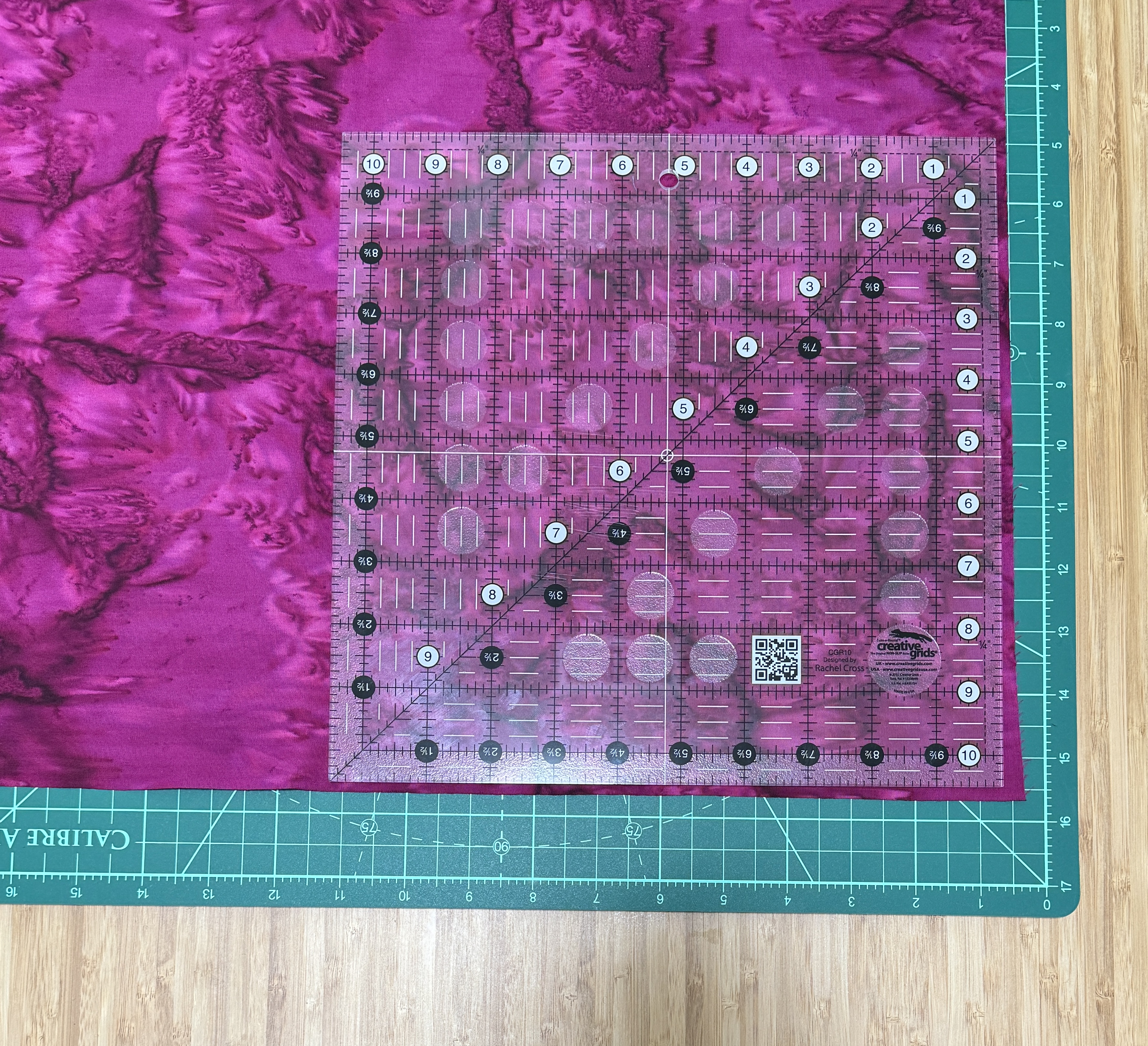 Purple batik fabric on a green swivelling cutting mat, with a 10.5 inch square ruler on top.