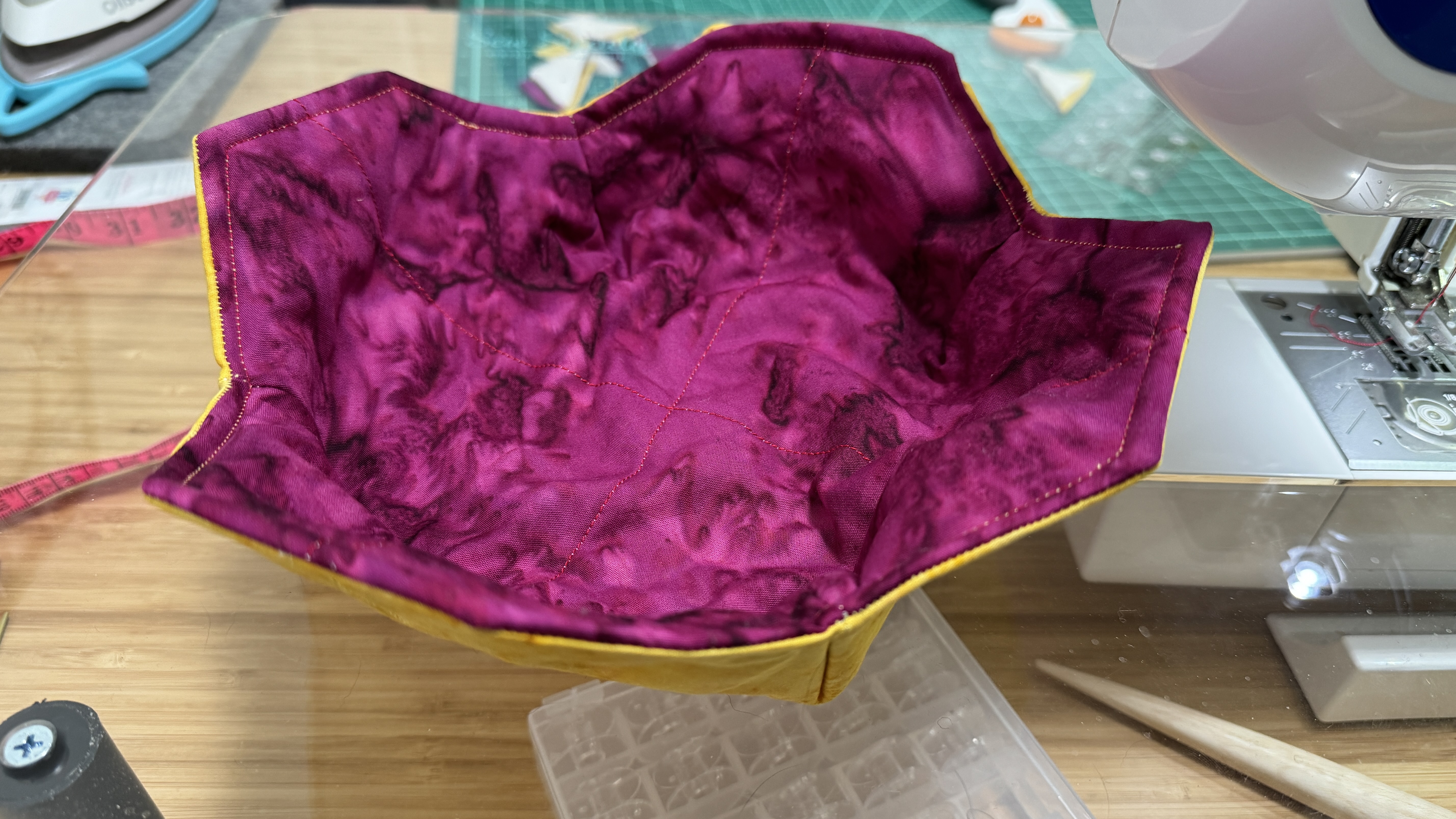 Bowl cozy next to my sewing machine. The inside of the bowl is purple. The edges of the cozy are scalloped.