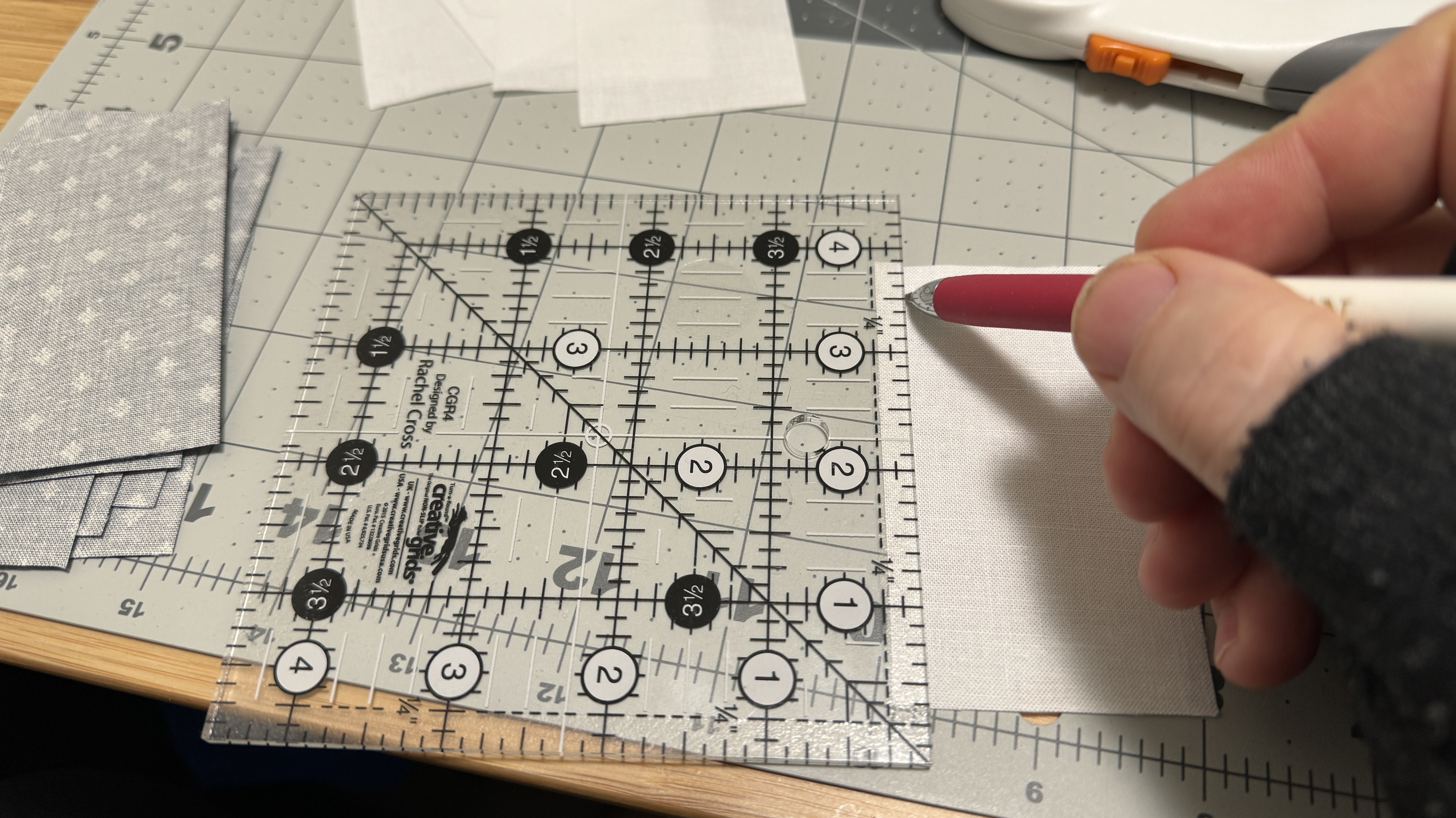 Quilting ruler marking a quarter inch on the fabric, and a mechanical pencil held in a hand, marking along the rulers length.