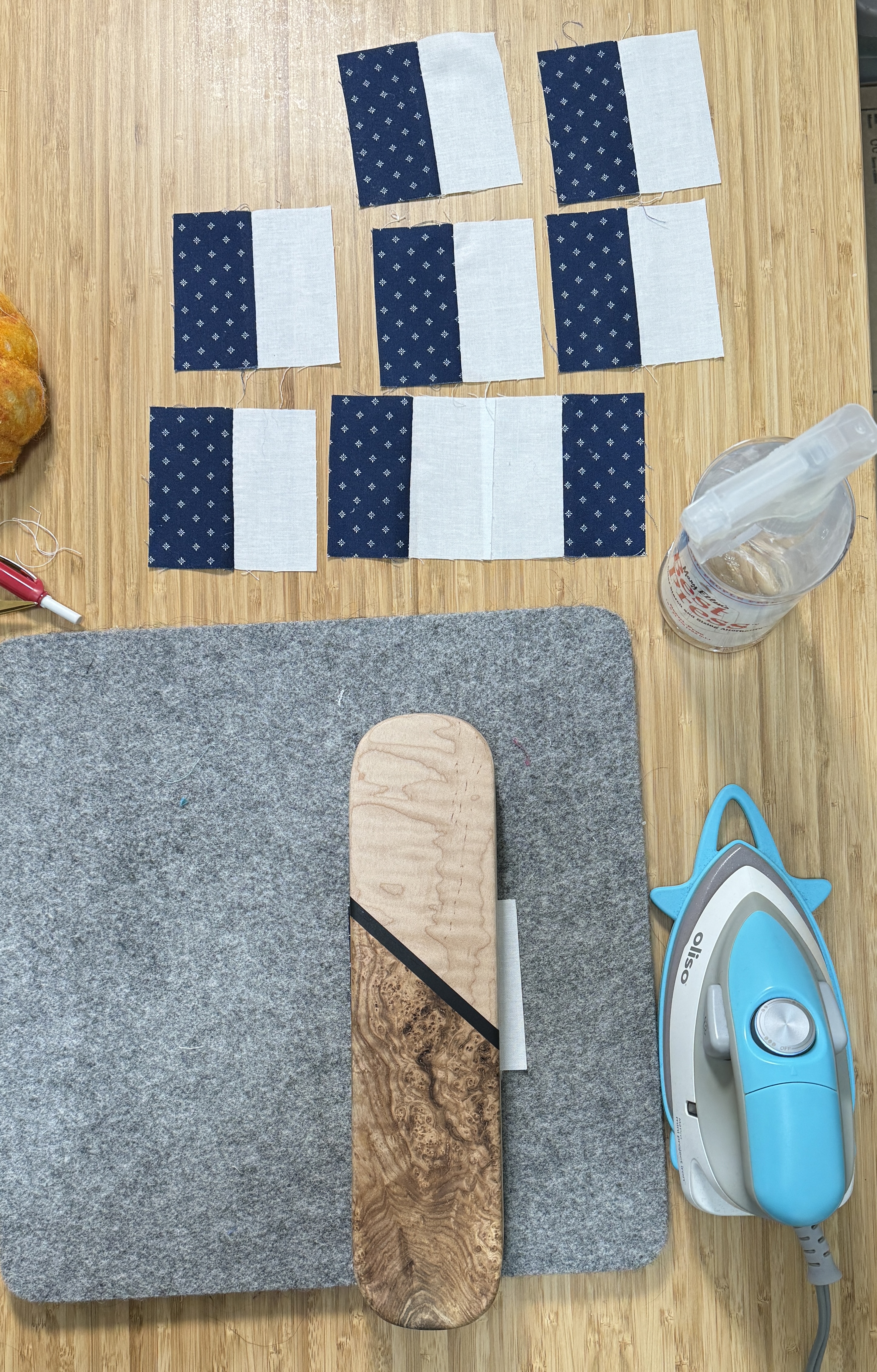 Eight completed chinese coins above a grey wool pressing mat. On the mat is a tailors clapper on top of the ninth chinese coin. The iron and Best Press bottle are nearby