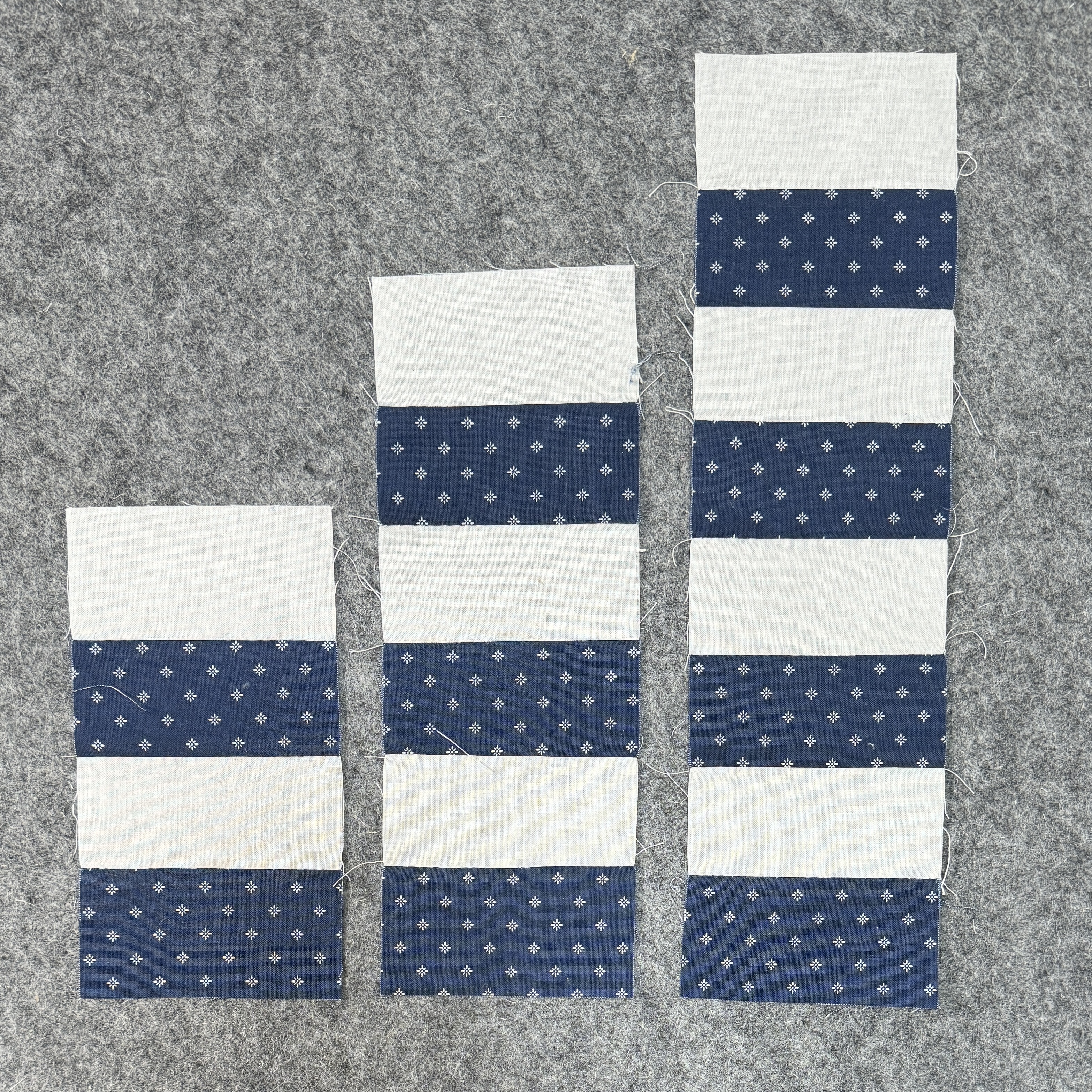 3 similar blocks. Off whife fabric rectangles stitched on the long side against navy blue fabric rectangles. One block has 4 rectangles. Another block has 6. The last one has 8.