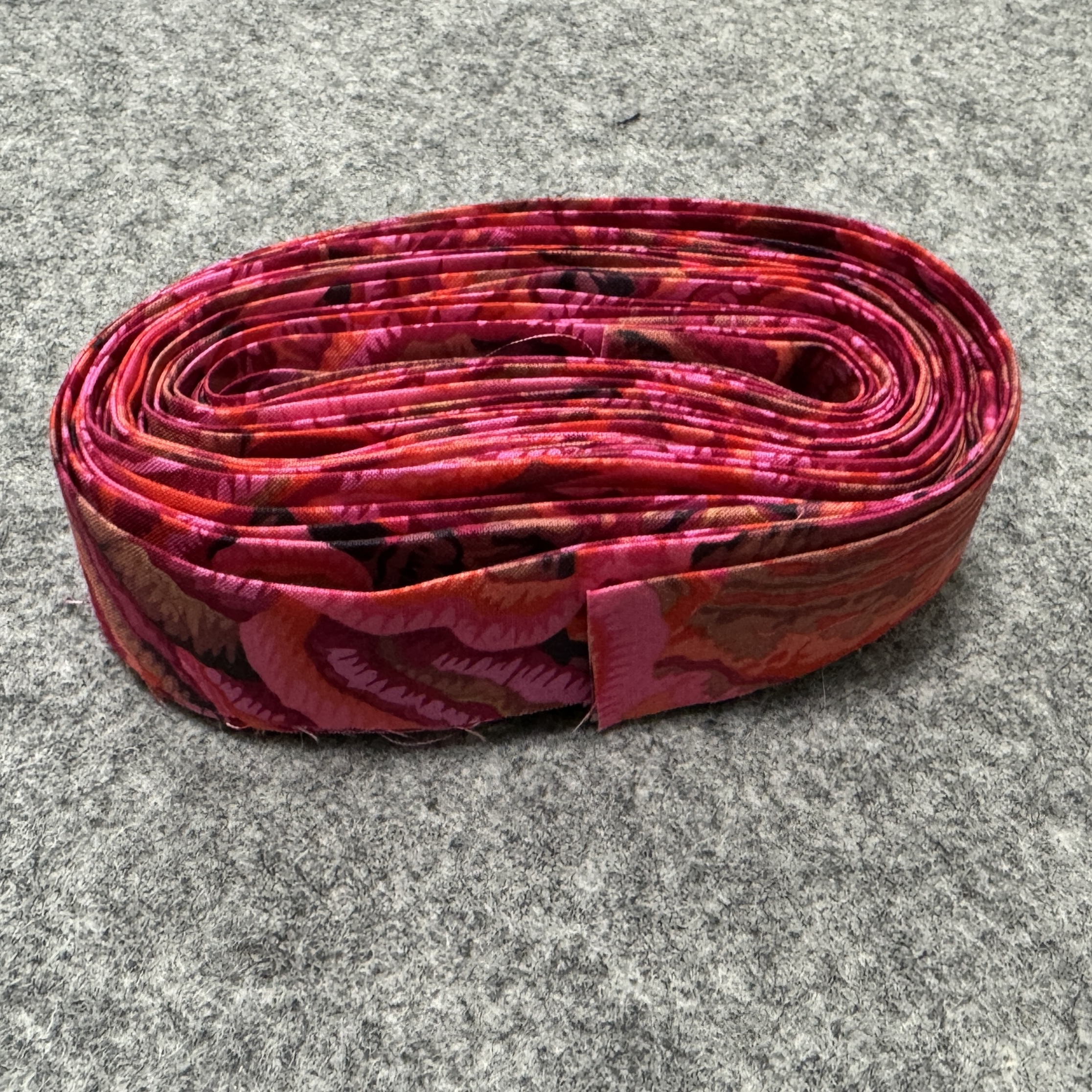Hot pink fabric cut into quilt binding, rolled, sitting on a grey felt mat.