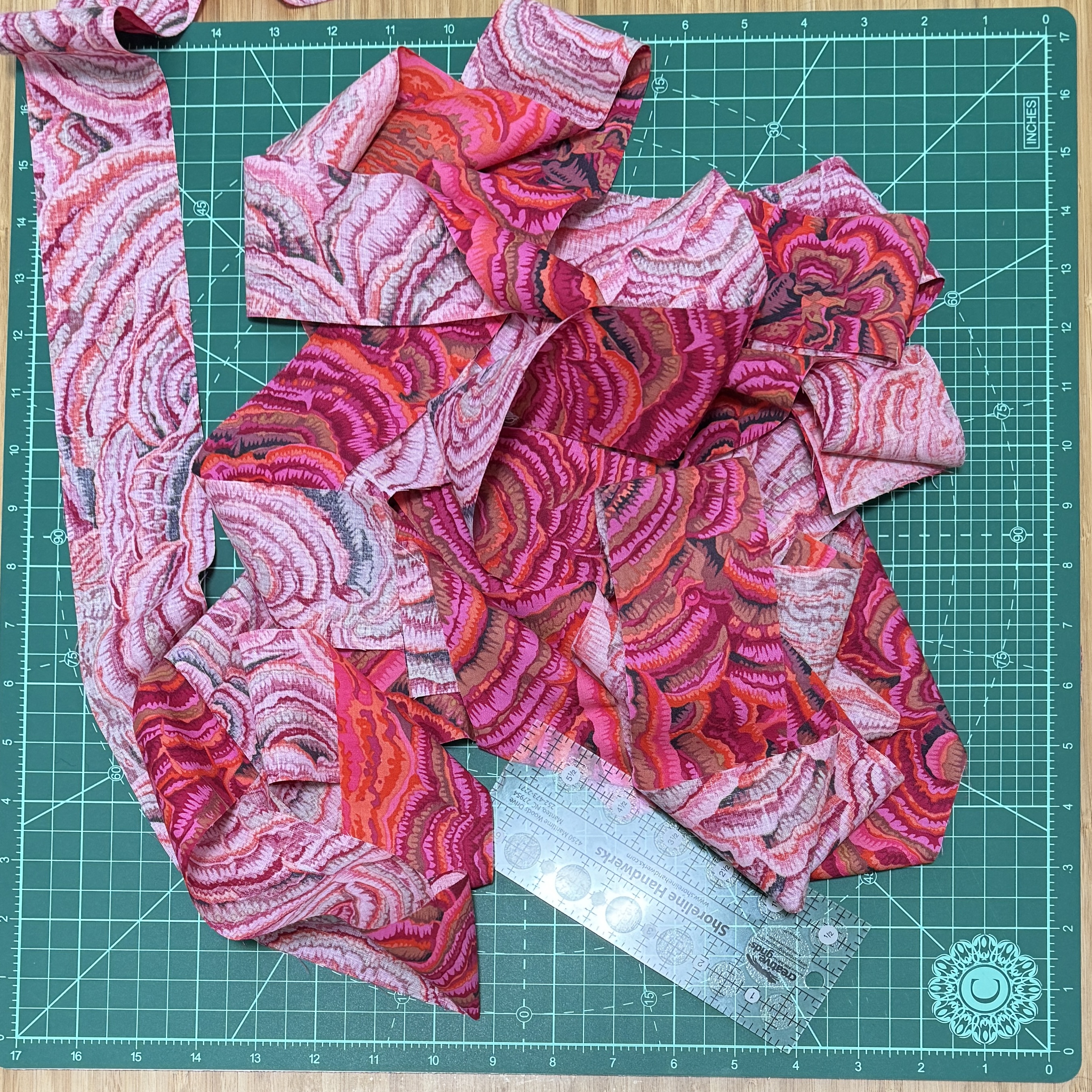 A two and a half inch long strip of hot pink fabric on a green cutting mat.