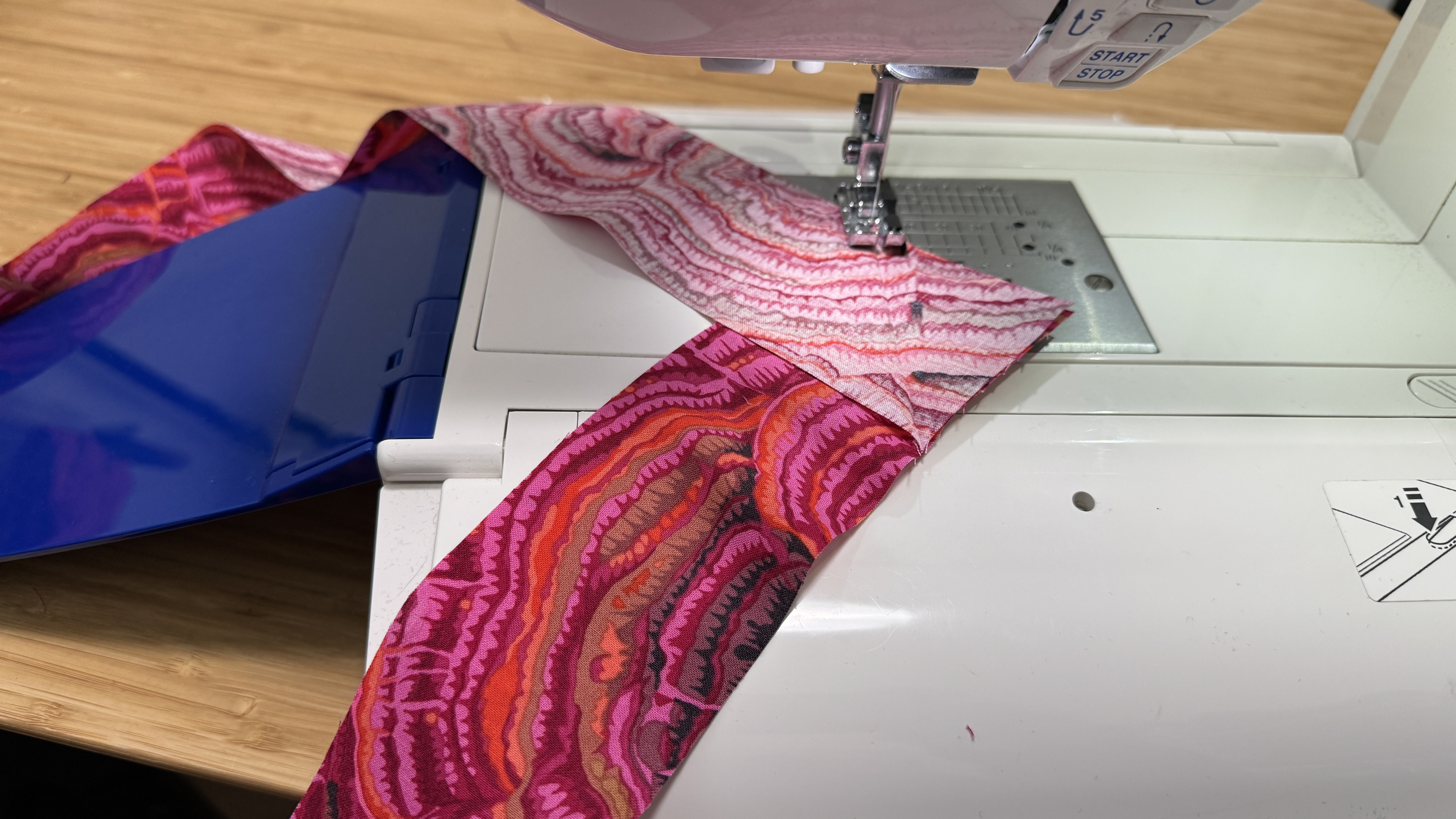 Two strips of hot pink fabrics, right sides together, being stitched at an angle on a sewing machine.