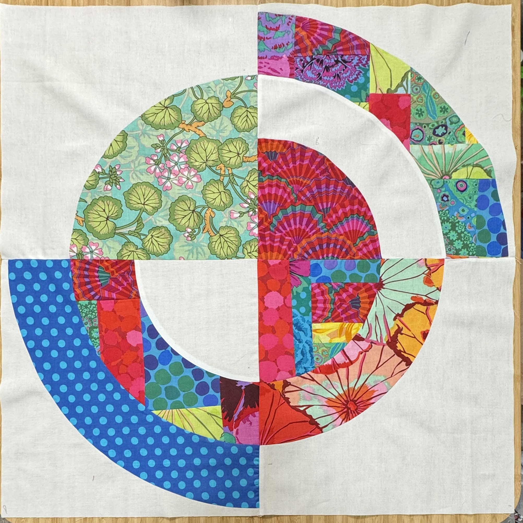 A large 24 inch square block of pieced fabrics in a riot of colors, shaped in nested circles.