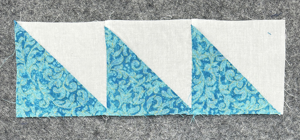 3 squares made of half square triangles, pieced in a line. Off white fabric for one set of triangles. Turquoise with a small leafy pattern for the others.