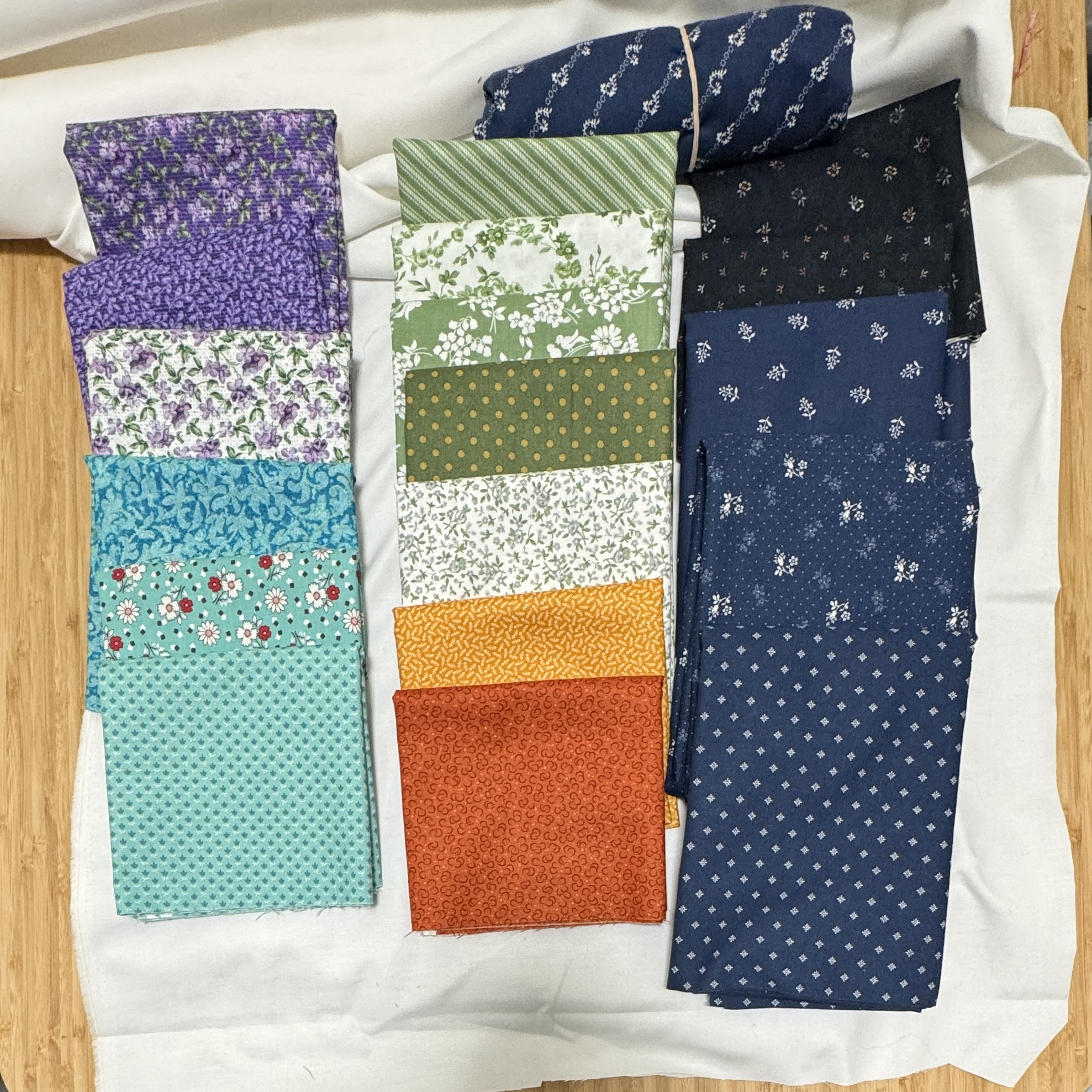 A bunch of different fabrics, mostly quarter yards, in blues, greens, lavenders, and oranges, all with different print patterns.