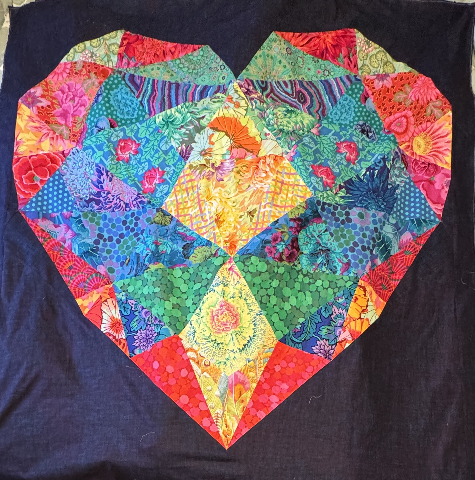 Colorful fabrics pieced in the shape of a heart, against a dark purple fabric