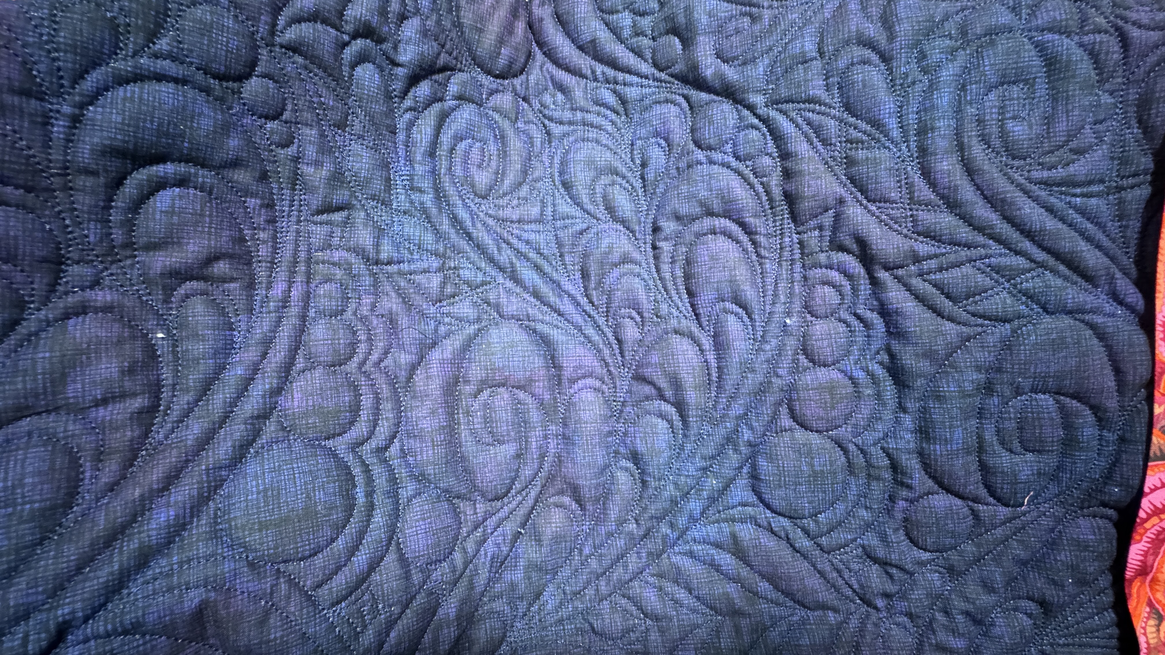 Intricate quilting on a dark purple part of a quilt.