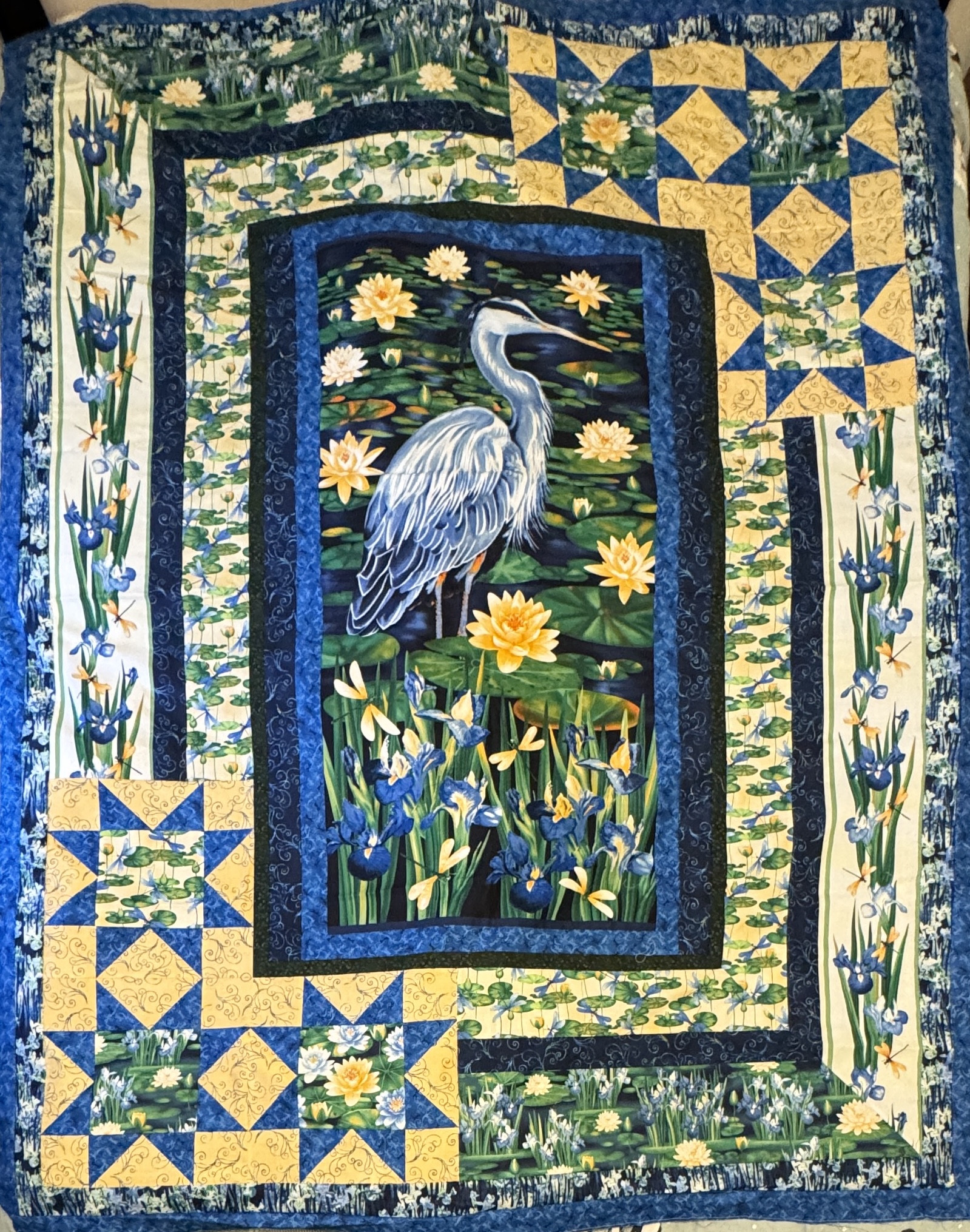 A large quilt top in blues, yellows, and greens, with a large center panel of a Great Blue Heron