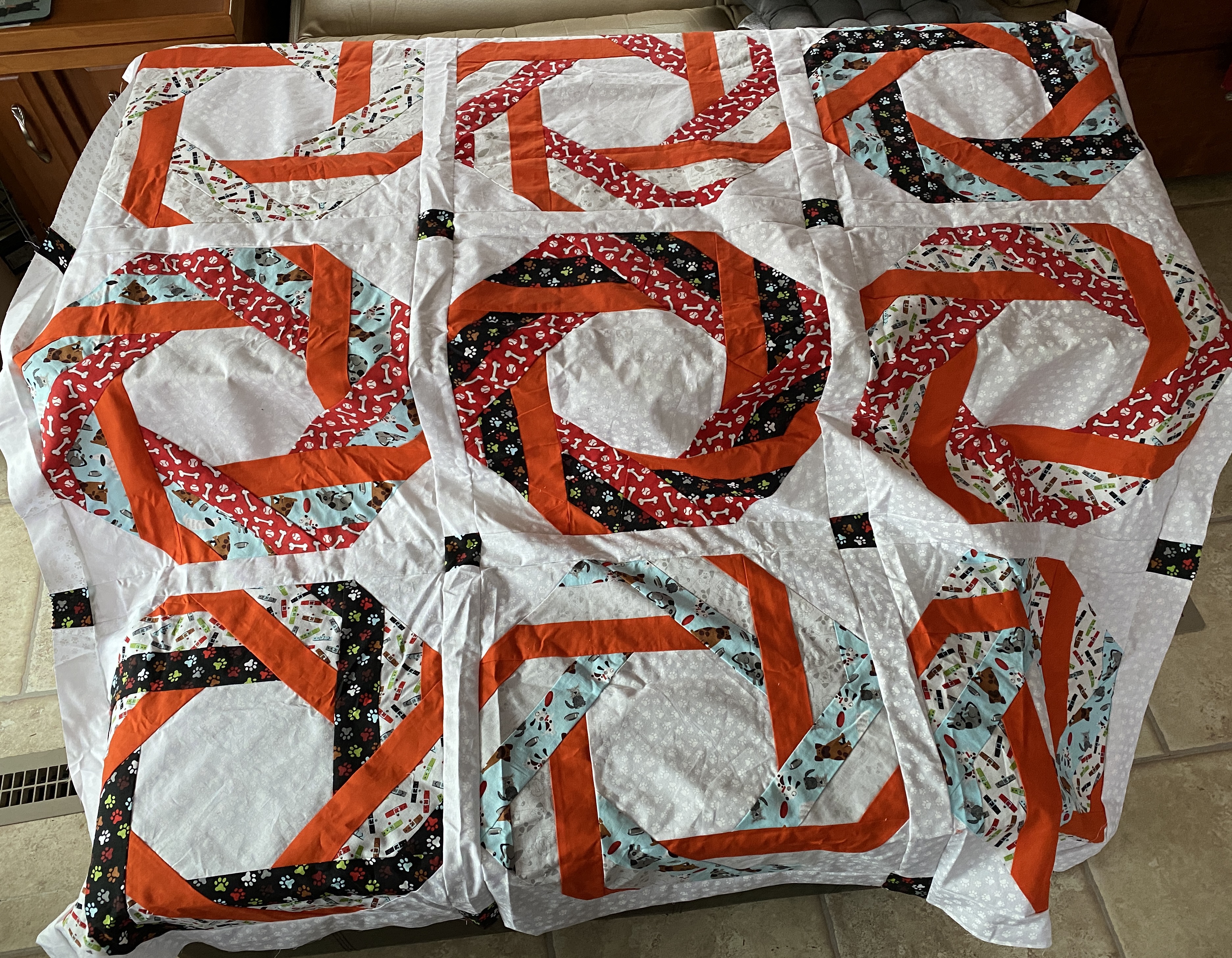 A quilt top with 9 blocks in 3 rows of 3 columns. Each block has a circular pattern of 2 inch strips, in reds, oranges, light blue, and black.