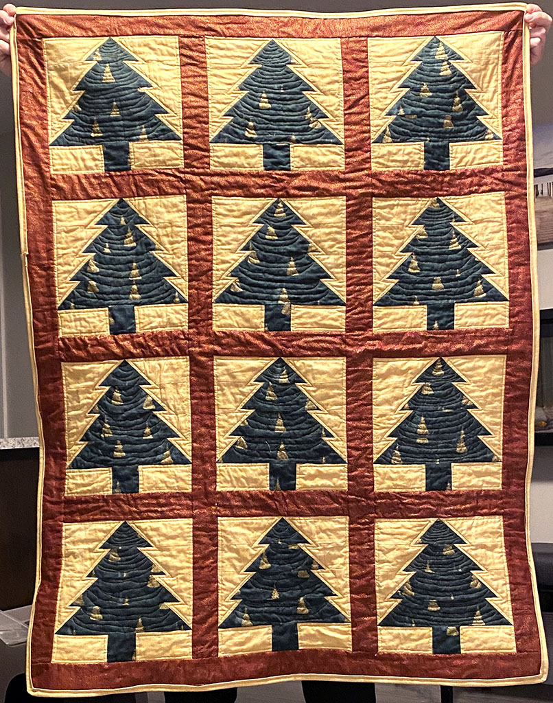 Lap sized quilt with 12 blocks in 3 columns of 4 rows. Each block is a green christmas tree on a yellow background, with red sashing and borders around all the blocks